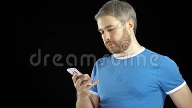 穿蓝色t恤的帅哥在黑色背景下<strong>点击</strong>他的智能手机<strong>触摸屏</strong>。 4K视频