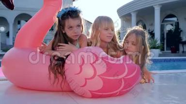 小女孩躺在游泳池附近的粉红色充气火烈鸟，孩子们在暑假穿泳衣的名人，被宠坏的富人