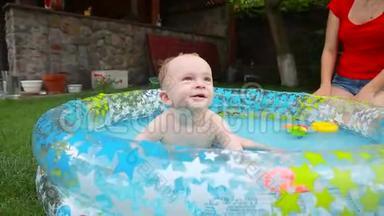 可爱的小男孩在花园草地上的充气游泳池里玩耍和泼水