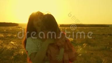 幸福的母亲和她的女儿在夕阳的照耀下抱在怀里散步。 妈妈在和快乐的宝贝说话，宝贝
