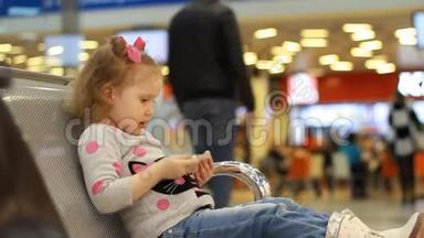 在机场候机楼里，坐在候机室里的孩子在等待他们的航班时玩手机。 A.