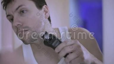 年轻迷人的男人在浴室里用电动剃须<strong>刀刮胡子</strong>。