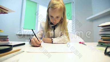 美丽的金发女孩穿着校服坐在桌子旁，用铅笔画画。