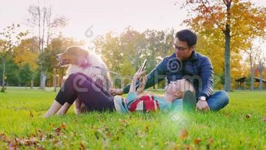异族青年夫妇和一只狗在公园里休息。 亚洲男人抚摸一只狗，白人女人看电子书阅读器