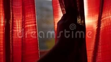女孩打开红色的窗帘，用手在阳光`的光线下玩耍。 手工特写