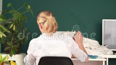 在家工作。 年轻的金发女人在明亮的房间里用打字机<strong>缝衣服</strong>