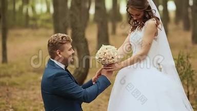 新郎给新娘一束她单膝站在大自然上的花。 快乐的新郎托起新娘围着她转。