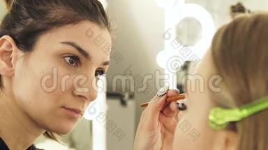 在化妆品工作室中，使用化妆刷在皮肤上化妆美丽的女人。 专业人员