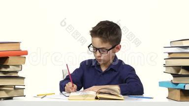 男孩坐在一张桌子旁，在她的笔记本上记录了一些东西，然后翻了翻书。 白色背景