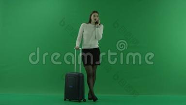女孩站在手提箱旁边，在绿色屏幕上打电话