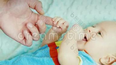 无忧无虑的婴儿<strong>两个</strong>月啃着他的<strong>拳头</strong>，握住父亲`手的手指。 躺在床上