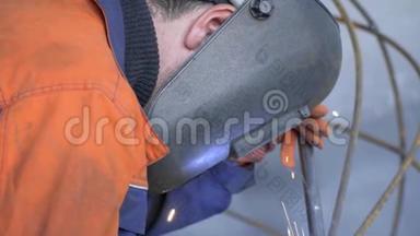 一个男人戴着防护面罩和橙色工作服，坐着一个铁架子，漏水，耀斑。 慢镜头拍摄