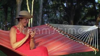 穿着红色衣服的女人<strong>坐在</strong>热带花园的红色吊<strong>床上</strong>。 普夸克岛的太阳能。 女人<strong>坐在</strong>