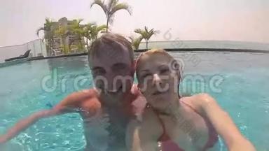 快乐的一对夫妇在游泳池里玩得很开心。 给朋友发信息。 暑假。 操作摄像机