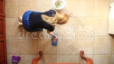 一个女人拿着一块蓝色的抹布在厨房里洗地板。 在五颜六色的桶里蘸一块抹布，从上面看