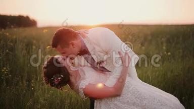 英俊的新郎把他美丽的新娘抱在怀里，亲吻她。 日落时在大自然美丽的地方举行婚礼