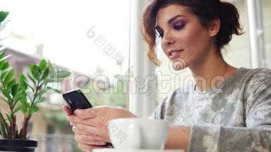 年轻迷人的女人在网上购物，用她的手机在咖啡馆里微笑。 在咖啡馆里使用智能手机的女人