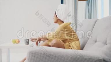 快乐的女人带着遥控器，洗澡后休息时选择<strong>电视频道</strong>。 头上是一条毛巾。