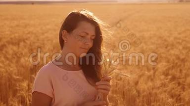 一个女孩在田野的肖像与小麦在日落剪影自然慢动作视频。 美丽的女孩在白田