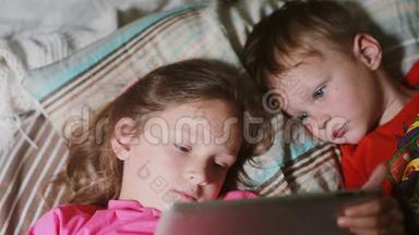 儿童一起躺在床上使用平板电脑的特写镜头。 女孩拿着平板电脑，男孩看卡通。