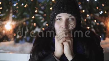 年轻迷人的女人用呼吸温暖她的<strong>双</strong>手站在圣诞树旁边。 新年<strong>庆</strong>祝理念