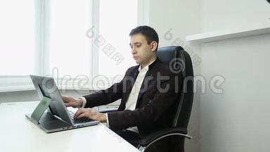 商人坐在桌子旁的办公椅上，在银色的笔记本电脑上打字。