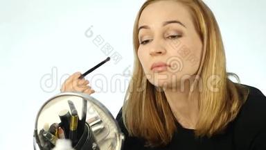 美丽的女人在小镜子前画眉毛，用化妆刷做日常化妆。 慢动作