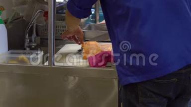 一家日本餐馆的厨师在一个开放的厨房里，用手剁肉，准备一个大鱼片