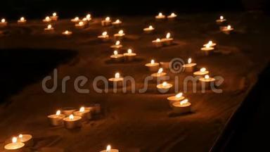 大量白色的小圆蜡烛在沙子里燃烧。 蜡烛燃烧的背景。