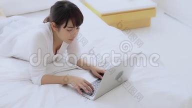 美丽的亚洲年轻女子躺在床上，在卧室里用手提电脑<strong>上网</strong>购物