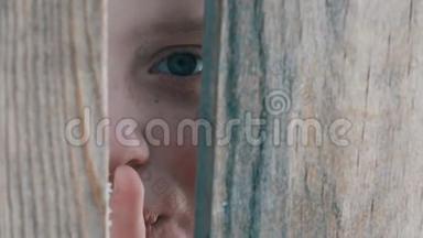 惊恐的少年男孩透过栅栏或<strong>门口</strong>的缝隙窥视，露出一根手指，表示沉默