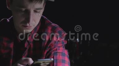穿着红色格子衬衫的疲惫和压力很大的年轻人厌倦了在黑暗的背景下用手机<strong>上网</strong>