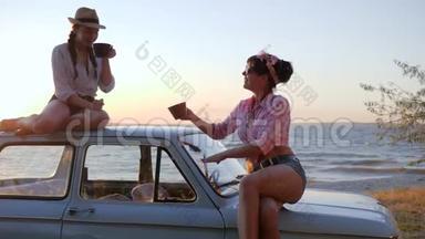 在日落时分，美丽的女孩在堤岸上的车篷上喝茶，女朋友喝茶