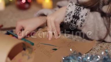 一个漂亮的小女孩在一棵装饰精美的圣诞树附近画了一幅圣诞老人的画。 特写镜头。 手工艺品