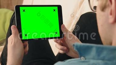 躺在沙发上看着绿色屏幕的数码平板电脑的年轻人