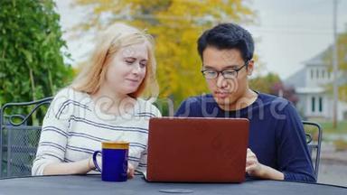 两个年轻的多民族朋友用笔记本电脑工作。 亚洲<strong>男人</strong>和高加索女人在<strong>夏季</strong>露台或咖啡馆