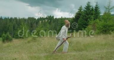 穿着旧衣服的老旅行者在<strong>拐杖</strong>的帮助下行走，拿着田野的花。 山的位置。