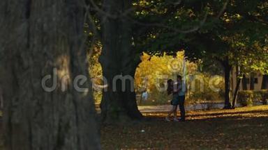 在秋天的城市公园里，一对年轻夫妇拥抱和亲吻对方的遥远景色。 几个进球。 浪漫浪漫