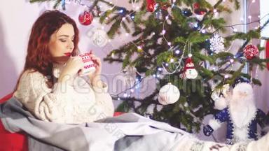 美丽的年轻女子穿着时尚的圣诞毛衣和袜子坐在舒适的沙发上喝茶的肖像。