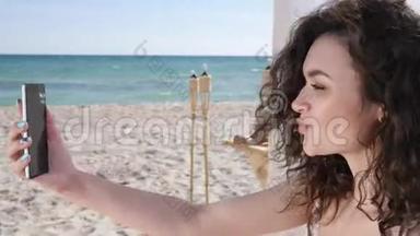 微笑的女孩在背景海洋和沙滩上自拍，在海滩上自拍的年轻女子，手机假日