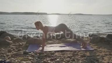 那个美丽的运动女子在海滨做早操。 海滩和日出的背景