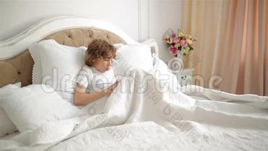 情感男孩正在用平板电脑玩电子游戏。 儿童床上有电子<strong>小东西</strong>的肖像。
