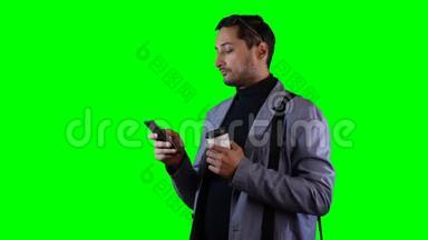 <strong>穿西装</strong>和黑色太阳镜<strong>的人</strong>使用移动和持有咖啡杯。 绿色屏幕，录像。