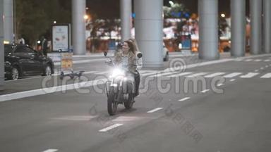 美丽的年轻女子摩托车手和他的女朋友骑摩托车在一个夜间城市的灯光街道。 两个骑自行车的女人