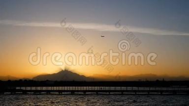 飞机飞过夕阳飞过高山.. 光线穿过黄昏的薄雾. 平静的大海和码头