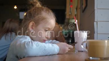 可爱的小女孩在咖啡馆里用智能手机。 快乐的孩子在放学后玩得开心和放松。 自然室内