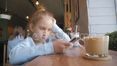 可爱的小女孩在咖啡馆里用智能手机。 快乐的孩子在放学后玩得开心和放松。 自然室内