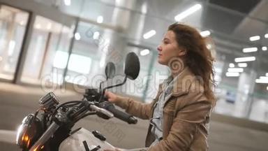 美丽的年轻女子骑着一辆古老的咖啡馆赛车摩托车在街上。 晚上的女自行车手。 慢动作