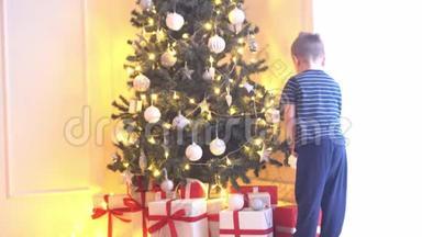 可爱的小男孩用球和灯装饰圣诞树。在家里准备过年的孩子。