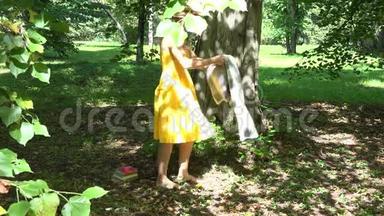 在阳光明媚的夏日，女孩坐在树下的格子上，在公园里看书。 4K
